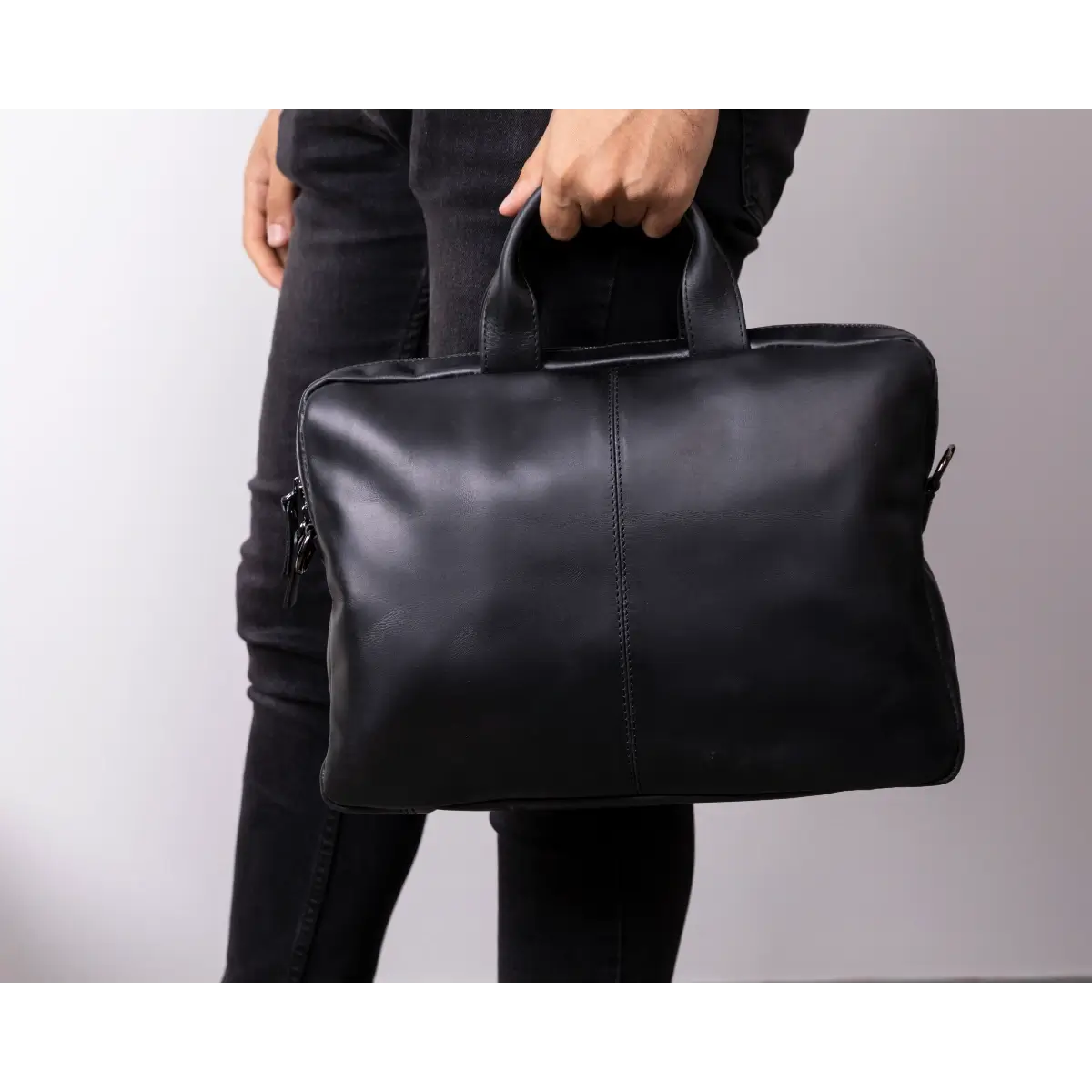 Person holding a black leather briefcase against a plain background