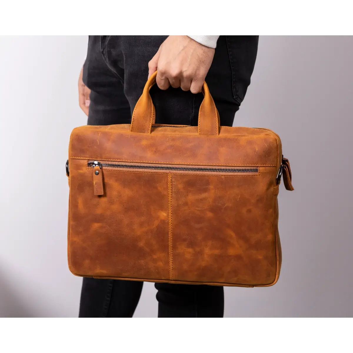 Brown leather briefcase held by a person against a plain background