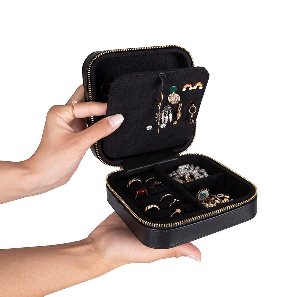 Black leather jewelry box with gold accents holding various earrings and rings, held open by a hand.